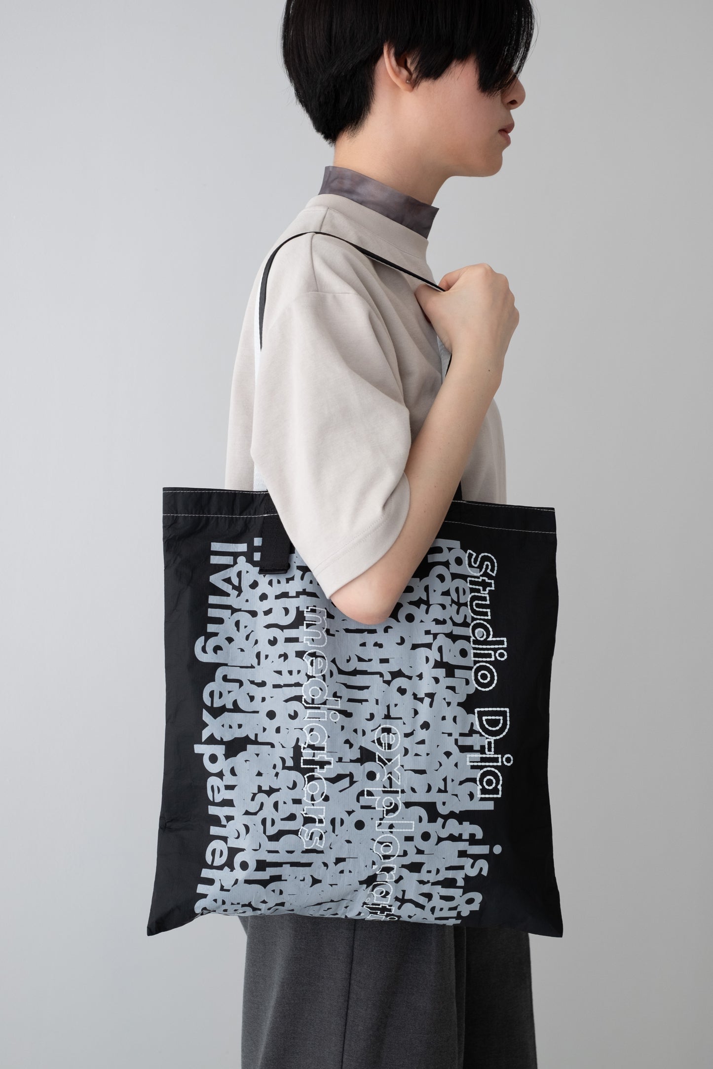 The D-ja Tote Bag worn over the shoulder, showcasing its expressive graphic print, asymmetrical handles, and lightweight yet durable design for everyday versatility.