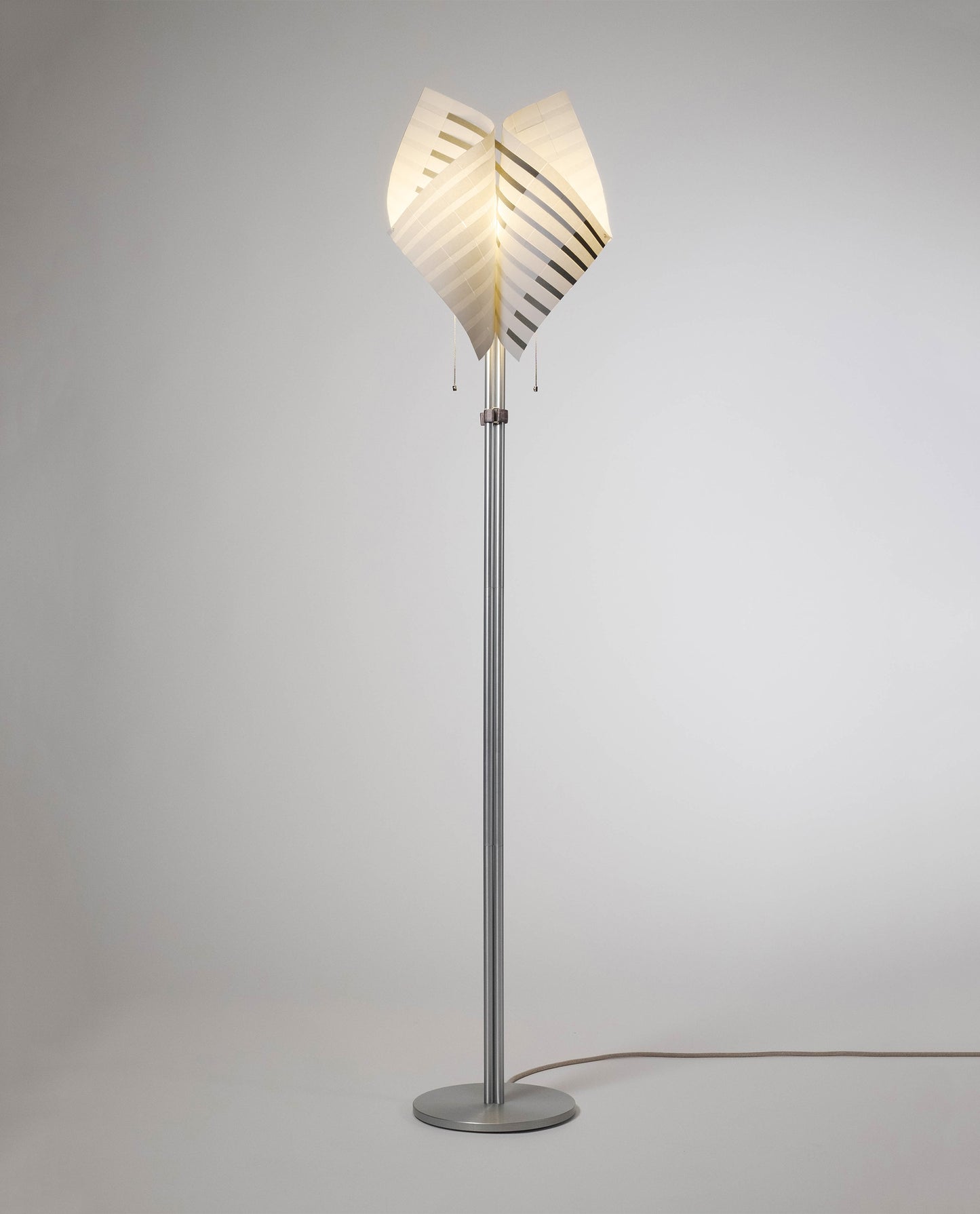 TEX001 floor lamp illuminated, showcasing its refined, symmetrical form and handwoven paper lampshade, blending sophisticated design with architectural elegance.